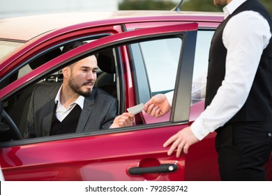 Valet Giving Receipt To Young Male Businessperson Sitting Inside Red Car