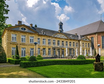 Valkenburg, South Limburg, Netherlands. May 14, 2023. Chateau St. Gerlach, backyard terrace with tables, chairs and closed umbrellas, green grass and bushes, view from a side angle