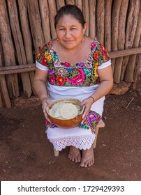 Valladolid, Yucatan/Mexico - February 26,2020: Mayan Women In Her Traditional Huipil Dress Holding A Bowl With Her Hand Made Tortillas In Front Of Her Wooden Pole Home
