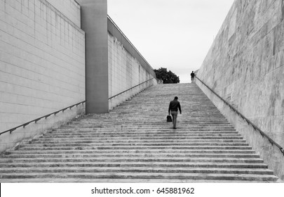 Valletta, MALTA - Business Man Walking In Valletta, Malta. Black And White Photo. One Man In The Street. Ambitions Concept With Businessman Climbing Stairs In Valletta, Malta. City Man.