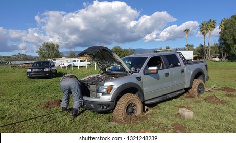 Valley Center, CA / USA - February 22, 2019: A Ford F150 Raptor Stuck In Deep Mud In A Field, Driver Working On Getting Pulled Out, Self Rescue With Built-on Winch                            