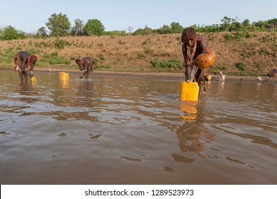 VALLEY OMO, ETHIOPIA - MARCH 15 2012: Unidentified women take a drinking water from the river Omo near Colcho, Omo Valley, Ethiopia. Muddy river water is only source of potable water for local people.