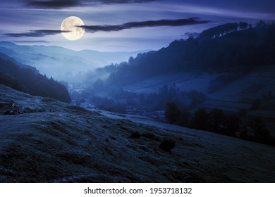 valley on the foggy night. village in the distance. grass and flowers on the hill in full moon light. beautiful countryside scenery. dark clouds on the sky - Powered by Shutterstock