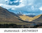 A valley in the Scottish Highlands,nestled between mountains with trees.The landscape shows a valley with clouds in the sky.The scenery showcases the beauty of the outdoor wilderness in the region