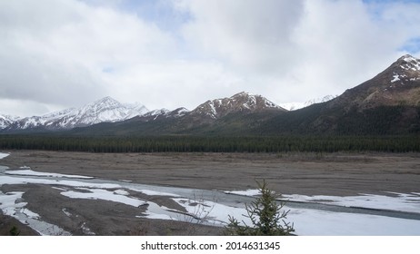 a valley with snow under clouds - aligned trees and snowy mountains in background