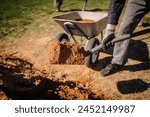 Valmiera, Latvia - April 21, 2024 - A person is shoveling soil into a wheelbarrow on a sunny day, showing a part of gardening or construction work.