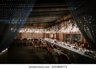 Valmiera, Latvia - August 10, 2023 - Elegant banquet hall with long dining tables, decorated with flowers and fairy lights, ready for a festive event. - Powered by Shutterstock