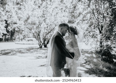 Valmiera, Latvia - August 15, 2024 - A romantic black-and-white photo of a bride and groom embracing under a veil, sharing an intimate moment outdoors. - Powered by Shutterstock