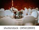 Valmiera, Latvia - August 19, 2023 - A warmly lit wedding reception hall with decorated tables, white chair covers, and a centerpiece with red and white flowers.