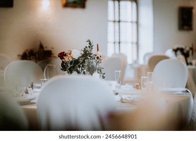 Valmiera, Latvia - August 19, 2023 - A softly focused wedding table setting with a lush floral centerpiece, red and white flowers, greenery, and elegant tableware under ambient lighting. - Powered by Shutterstock