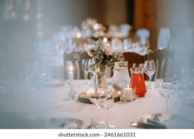 Valmiera, Latvia - August 25, 2023 - Close-up view of wedding reception table with a floral centerpiece, lit candles, and drinks on a white tablecloth. - Powered by Shutterstock