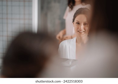 Valmiera, Latvia - July 7, 2023 - A smiling woman in a white robe being attended to by another, reflected in a mirror. - Powered by Shutterstock