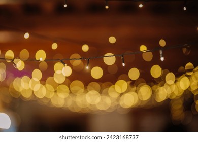 Valmiera, Latvia - July 7, 2023 - Focused string lights with blurred golden bokeh effect against a dark backdrop. - Powered by Shutterstock