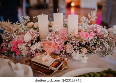 Valmiera, Latvia - July 7, 2023 - A floral wedding centerpiece with pink flowers and white candles on a table, with a matchbox and blurred background.