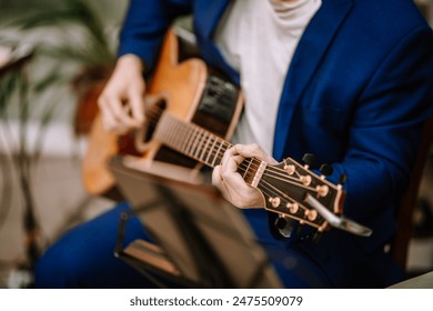 Valmiera, Latvia - September 9, 2023 - A close-up of a musician in a blue suit playing an acoustic guitar, with a music stand in the foreground and a blurred background. - Powered by Shutterstock