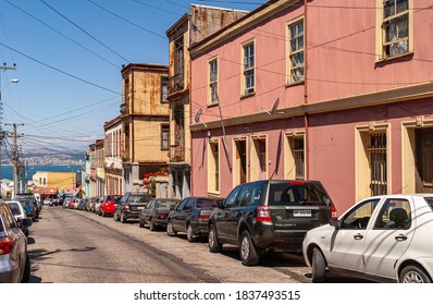 Valparaiso, Chile - December 8, 2008: Lower Middle Class Neighborhood Street With A Few Houses And Cars Parked In Front Under Blue Sky. The Blue Water Of The Bay Is Visible In Distance.