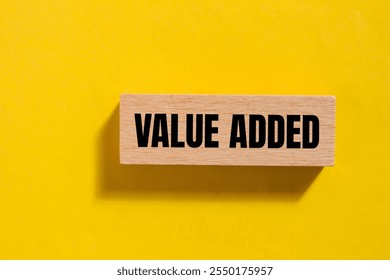 Value added message written on wooden block with yellow background. Conceptual value added symbol. Copy space.