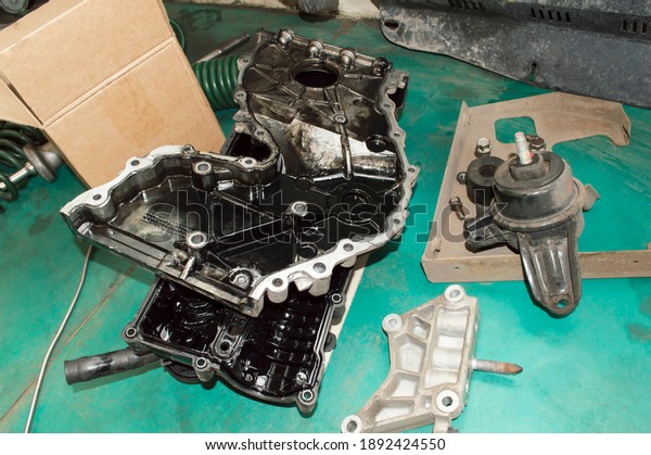 The valve\
cover and front covers of the internal combustion engine lie on the\
green floor in the auto repair\
shop