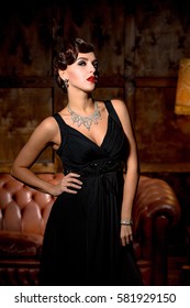 Vamp lady with red lips posing for photographer in restaurant. Elegant lady in black dress posing with her hand on hip.