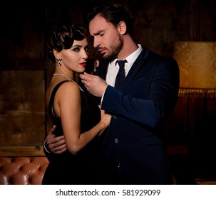 Vamp woman with red lips looking at camera and dreaming about marrying millionaire man. Handsome businessman hugging lady and touching her chin.