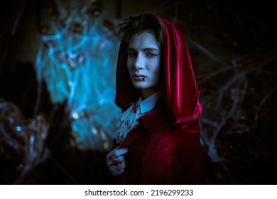 Vampires. Portrait Of A Handsome Young Vampire Standing In His Abandoned Castle In An Elegant 19th-century Clothes And Red Velvet Cloak. Halloween. 