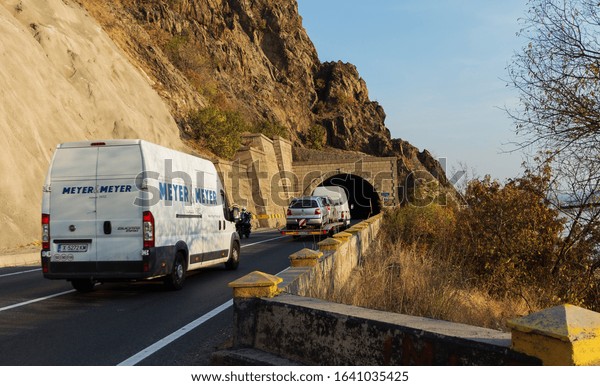 Van and cars transported on the car platform on a\
beautiful mountain road, at the entrance to the tunnel. Van Meyer\
& Meyer. Auto transport trailer. Cars in traffic. Severin,\
Romania, November 9, 2019