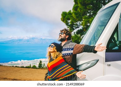 Van Life And Travel Destination Concept. Man And Woman Excited For New Arrival In The Nature Opening Arms Against Their New Modern Motor Home Camper. Free Camp Site With Rv. People Living Off Grid