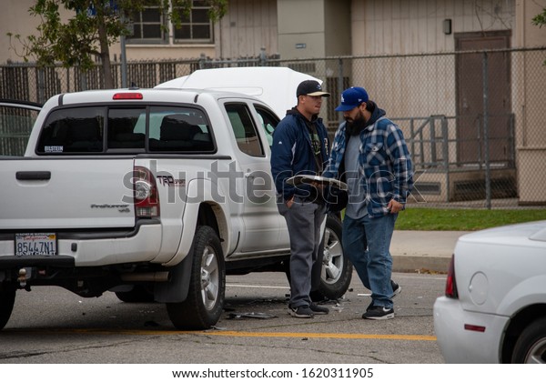 Van Nuys,\
California / USA  - January 19, 2020: The driver and passenger\
clean up debris from a white Toyota Tacoma truck sitting in the\
middle of the road after an\
accident.