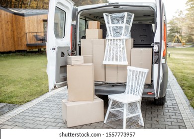 Van Vehicle Trunk Full Of Boxes And Furniture Near A House Outdoors. Concept Of Moving To A New Home And Delivery