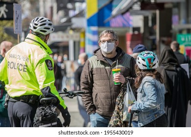 Vancouver, BC, Canada, 04.11.2021 Vancouver Police Officer Is Talking To The Male Pedestrian In The Mask, Holding A Drink, A Child In A Helmet Is Standing With A Back To The Camera, The Street View