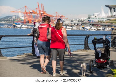 Vancouver, BC, Canada, 7 01 2022,  Two Women In The Red Tops Are Walking In The Street With A Blurry Port On A Background During The Canada Day Celebrations In Downtown