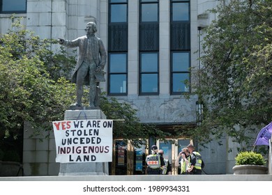 Vancouver, BC, Canada - June 12, 2021: Vancouver Police Officers Talk Behind A Statue Of George Vancouver Covered In A Sign Recognizing Indigenous Land Rights 