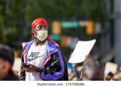 Vancouver BC, Canada, May 31 2020: Portrait Of A Young Men With A Face Mask And A Red Cap Looking Away Into The Crowd Above Everybody With Blurred Crowd Behind Him, At A Rally