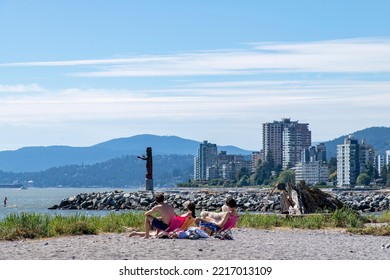 Vancouver, BC, Canada-August 2022; Close Up View Of Some Young People On Ambleside Beach In West Vancouver And Squamish Nation Welcome Figure In Background On A Sunny Day