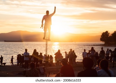 Vancouver, British Columbia, Canada - June 26, 2021: Talented Street Performer Doing A Show With A Unicycle In Front Of A Large Crowd Of People On The Beach During Sunny Summer Sunset.