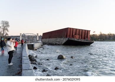 VANCOUVER, CANADA - 11-16-2021 - People walking in front of the Beached Barge on Sunset Beach 
 with Burrard Street Bridge in the background after a devastating storm the previous day