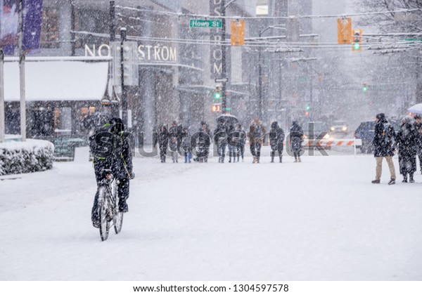 Vancouver,\
CANADA - 23 Feb, 2018 : man is riding bicycle in hurry to delivery\
stuff while it has heavy snow storm. People walking  on Robson\
Square, Downtown Vancouver when it\'s\
snowing.