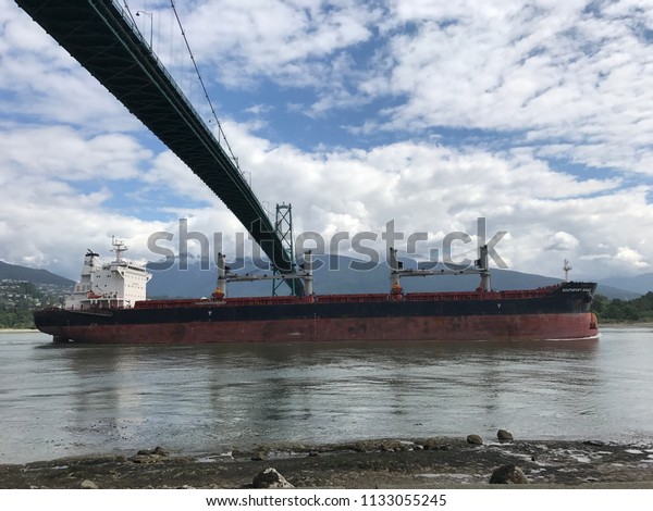 Vancouver, Canada / June 4, 2017:\
Stanley Park Seawall and Lions Gate Bridge, Vancouver, British\
Columbia, Canada.  A large cargo sheep passing under the bridge.\
