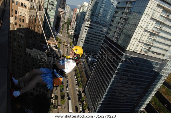 VANCOUVER, CANADA - SEPTEMBER 10, 2014: A woman\
climbs down office building during Easter Seals Drop Zone\
fundraiser to benefit children with disabilities in Vancouver,\
Canada, on September 10,\
2014.