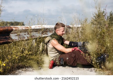 vandal man in dirty clothes sits on an abandoned grassy road, on a bridge