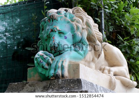 Vandalized statue of a sad lion. Sad green colored face with spray paint