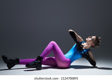 Vanguard fashion. Full-length portrait of a model girl posing with expression in bright extravagant clothes against a gray studio background. Black makeup and avant-garde hairstyle.