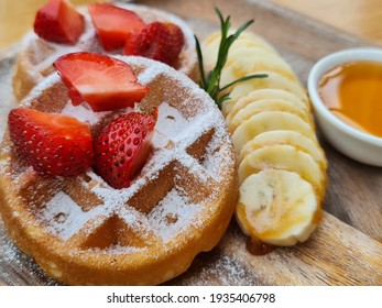 Vanila waffle with banana topping with straberries icing sugar and maple or honey syrup on wooden plate and table