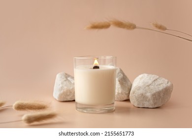 Vanilla burning candle on beige background. Warm aesthetic composition with stones and dry flowers. Home comfort, spa, relax and wellness concept. Interior decoration