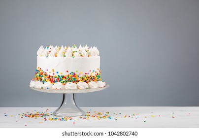 Vanilla buttercream Birthday cake with colorful sprinkles over a neutral background.