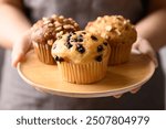 Vanilla chocolate chips muffin, Chocolate almond muffin and Vanilla almond muffin on wooden plate holding by hand