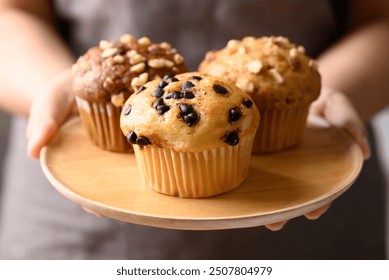 Vanilla chocolate chips muffin, Chocolate almond muffin and Vanilla almond muffin on wooden plate holding by hand