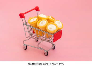 Vanilla Cream In Wafer Cup In A Shopping Cart A Small Toy. Vanilla Ice Cream Cone On Pink Color Background. Candy Bar And Cake Pops. Holiday Treats. Sweet Tooth. Candy Shop. 