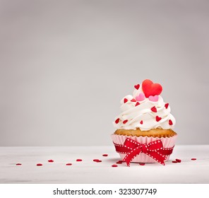 Vanilla Cupcake With Buttercream Icing, Heart Shaped Sprinkles And A Red Bow.