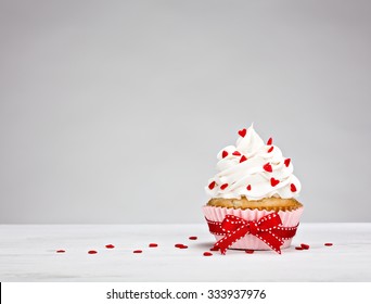 Vanilla Cupcake With Buttercream Icing, Heart Shaped Sprinkles And A Red Bow.